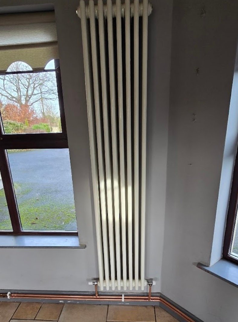 Tall white column radiator with copper pipe base connections
